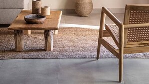 A living room with a grey sofa, a wooden coffee table with decorative items, a woven basket, and a woven vase on a rug. - Nomada 1 | Chania City Center (Chania)