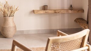 A living room with a wooden chair, a woven floor rug, a woven vase with dried plants, a wooden shelf with a candle, and a flat-screen TV mounted on the wall. - Nomada 1 | Chania City Center (Chania)