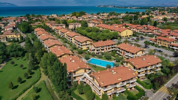 An aerial view of a residential area with multiple apartment buildings, a swimming pool, and a view of the sea.