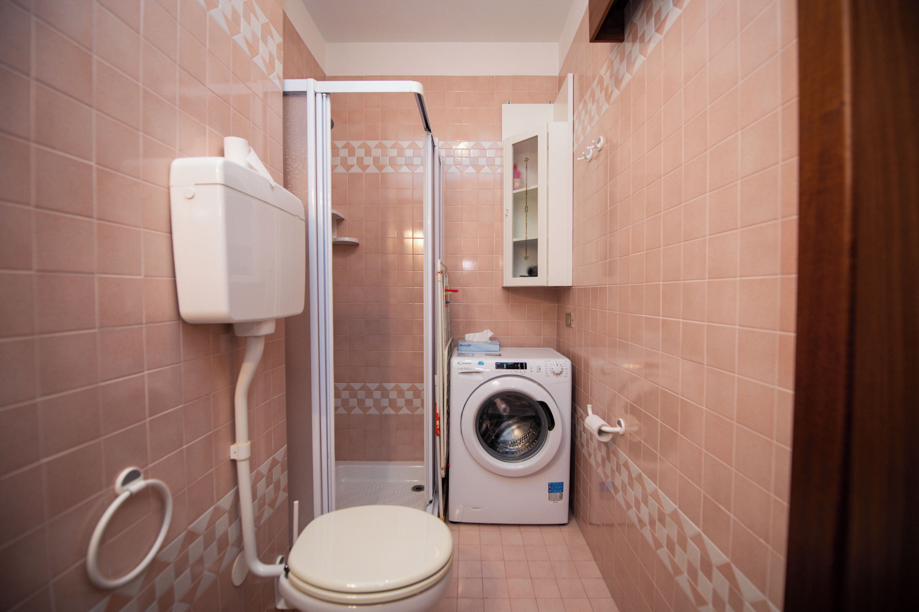 A compact bathroom with a toilet, a washing machine, and a shower enclosure.