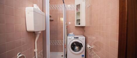 A compact bathroom with a toilet, a washing machine, and a shower enclosure.