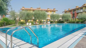 A swimming pool with metal railings, surrounded by greenery and buildings with yellow and red facades.