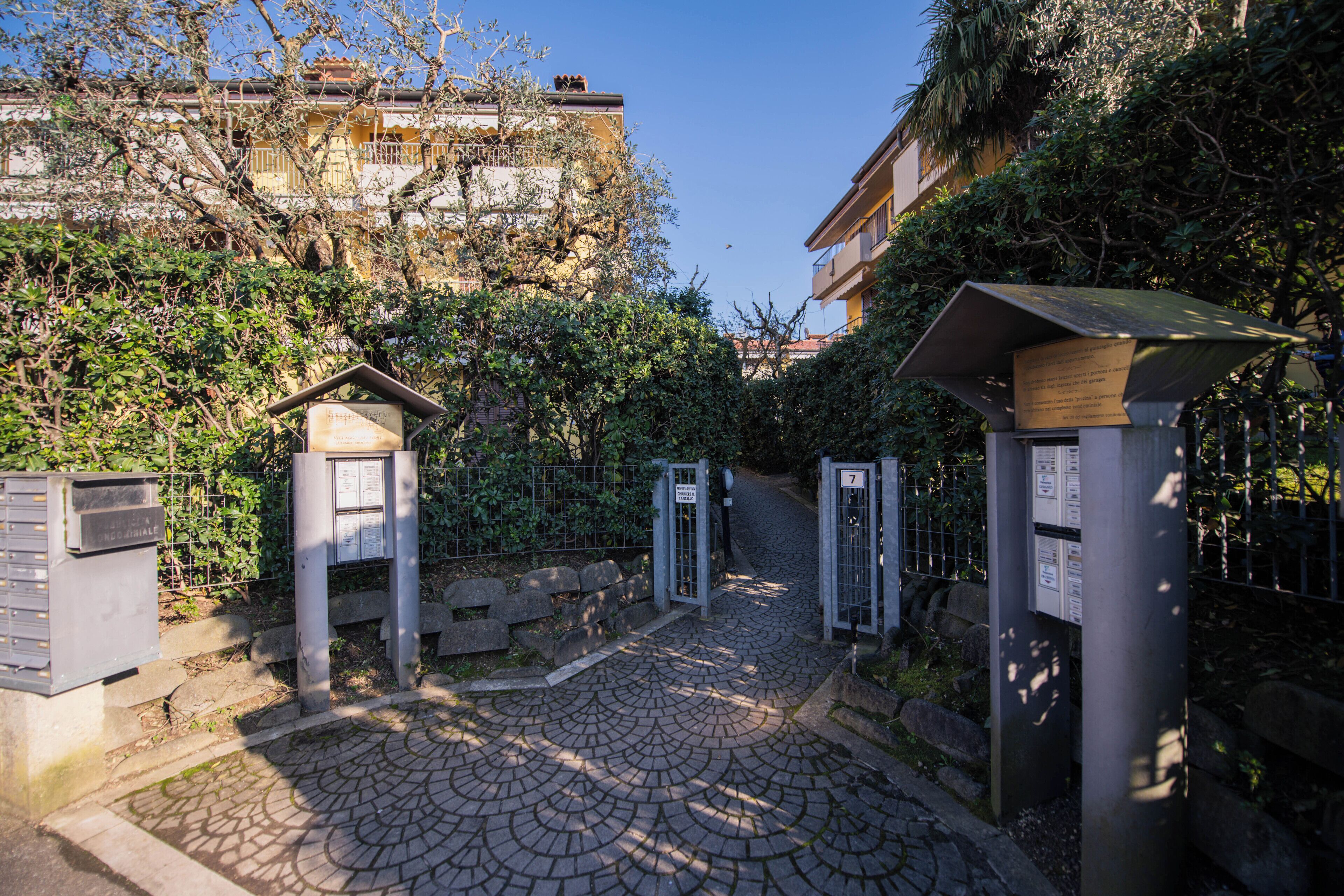 A cobblestone pathway leading to a gated entrance with a metal gate and a small shelter.