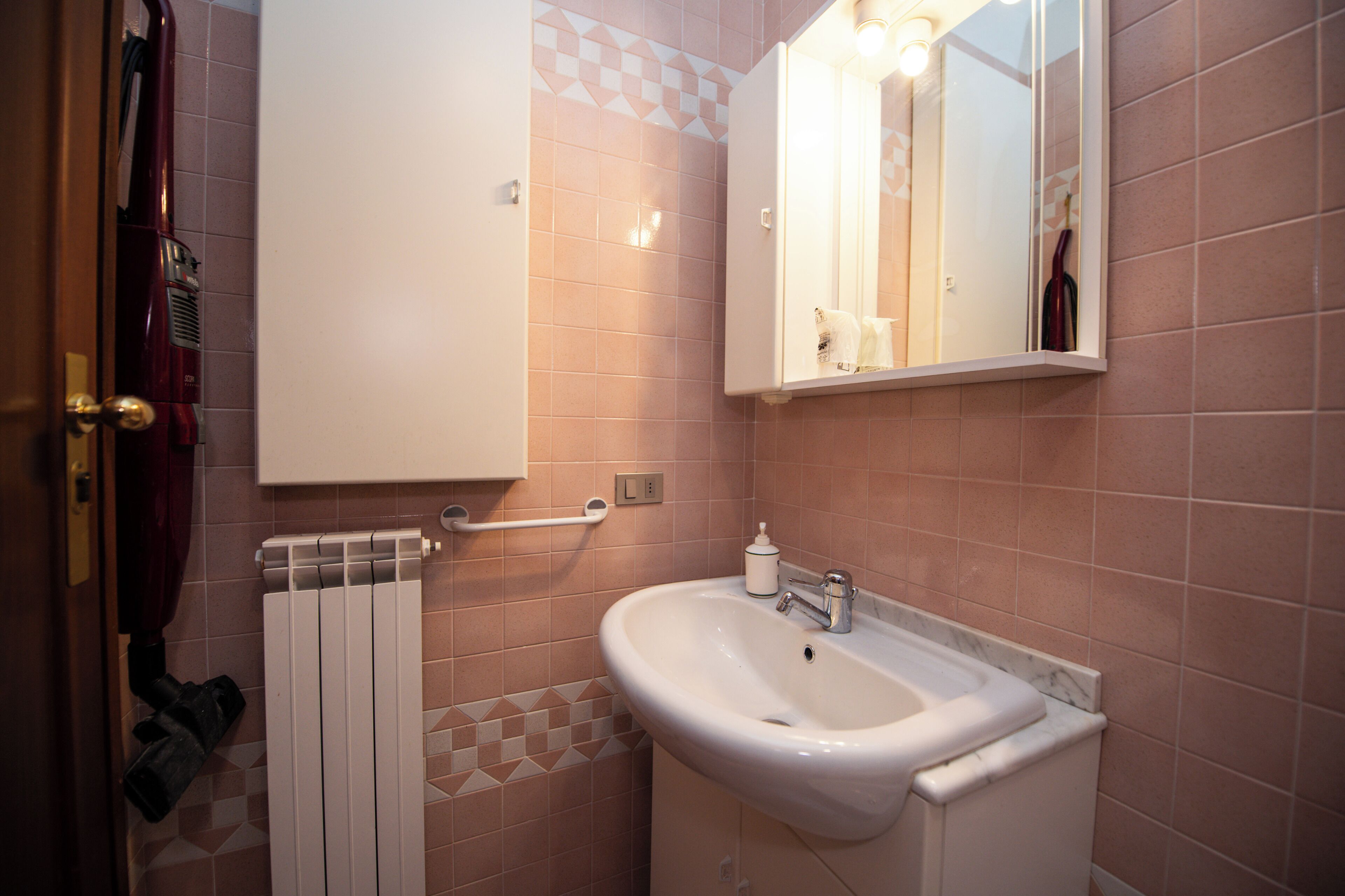 Un bagno con un lavandino bianco, uno specchio e un porta asciugamani.