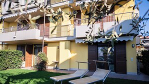 A yellow building with balconies, a small lawn, and two lounge chairs.