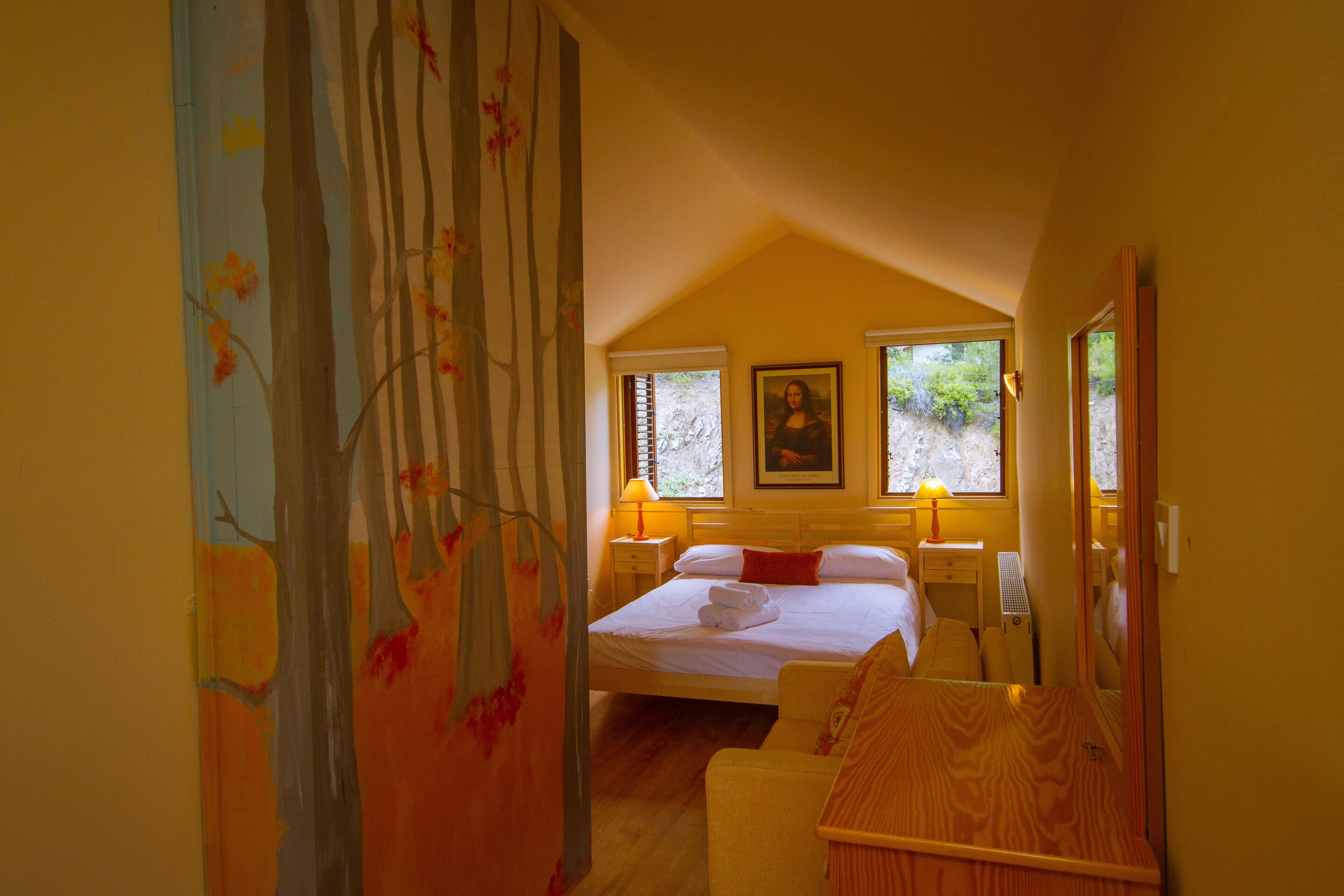 Un dormitorio con cama, mesitas de noche, una silla y una ventana.