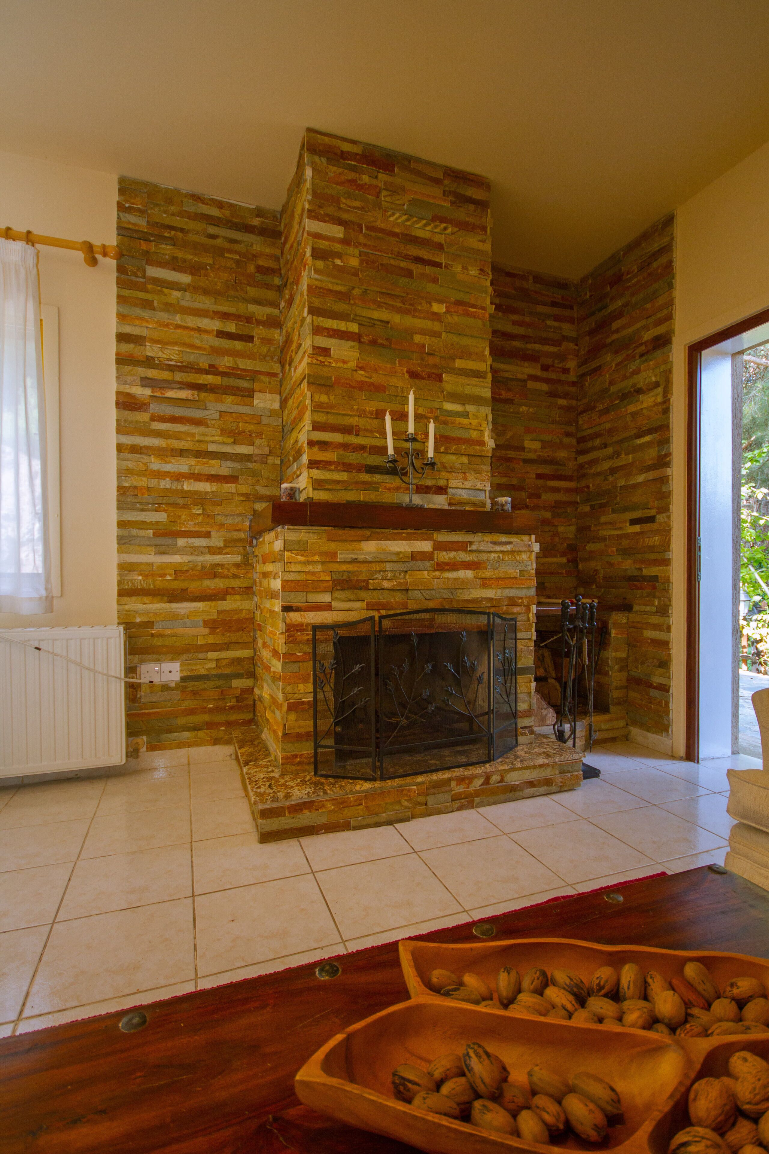 Un salón con chimenea de piedra, una mesa de madera con cuencos de nueces y vistas al exterior con vegetación.