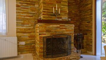 Un salón con chimenea de piedra, una mesa de madera con cuencos de nueces y vistas al exterior con vegetación.