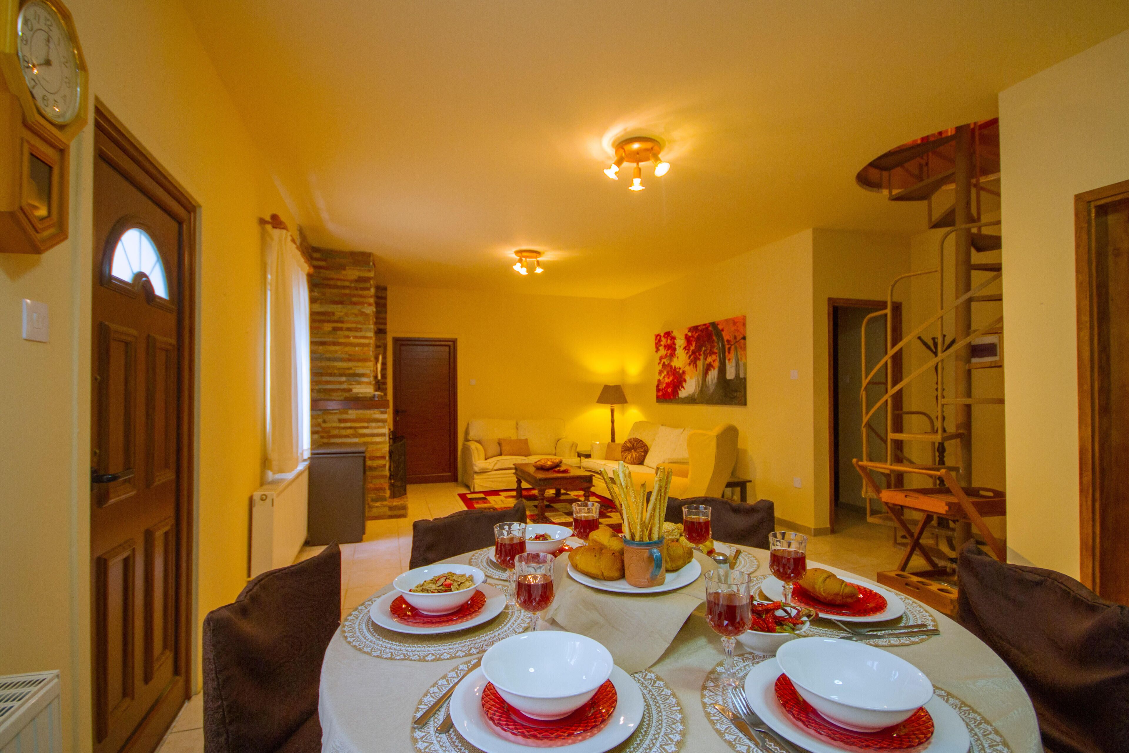 Un comedor con una mesa dispuesta para una comida, una escalera y una sala de estar al fondo.