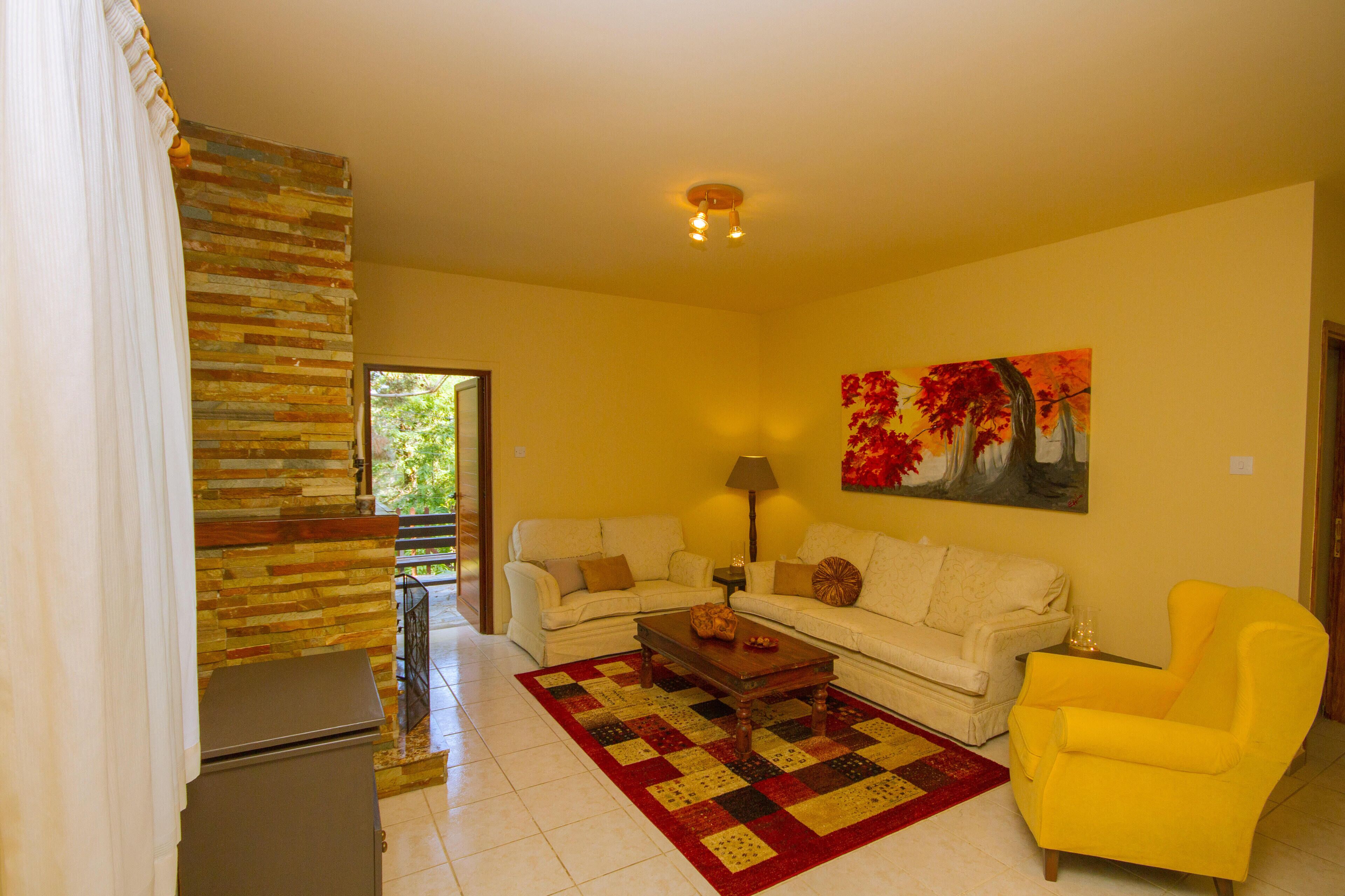 A living room with two sofas, a coffee table, a yellow armchair, a painting, and a stone wall.