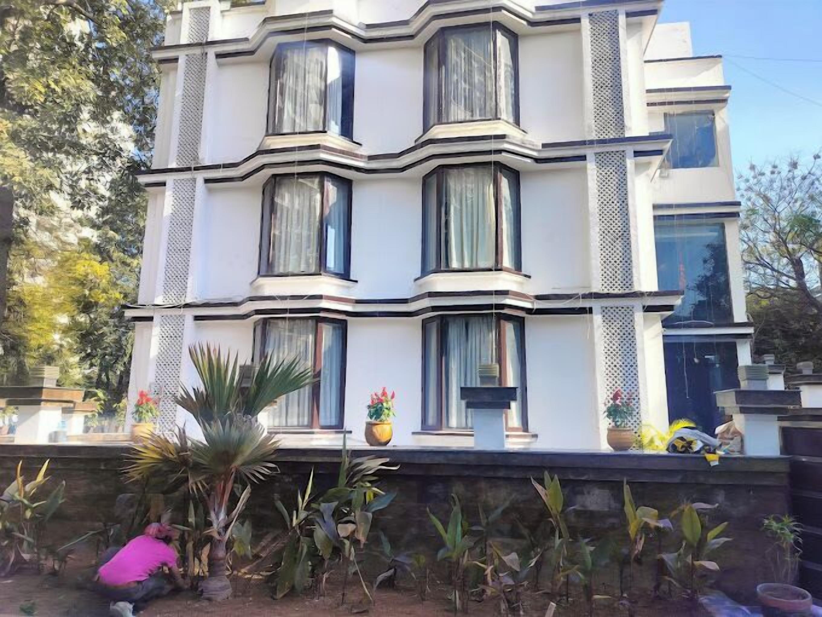 A multi-story building with a modern architectural design, featuring large windows and a balcony with potted plants.