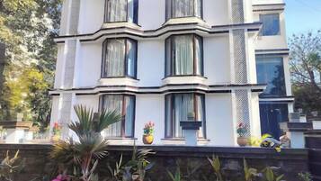Um edifício de vários andares com um design arquitetônico moderno, com grandes janelas e uma varanda com plantas em vasos.