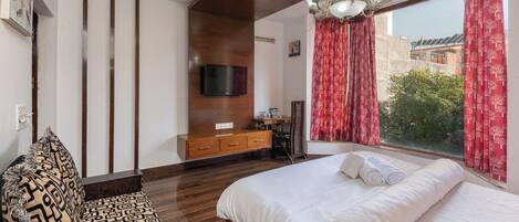 Une chambre moderne avec un grand lit, un plafond en bois, un téléviseur fixé au mur et une vue sur la verdure.