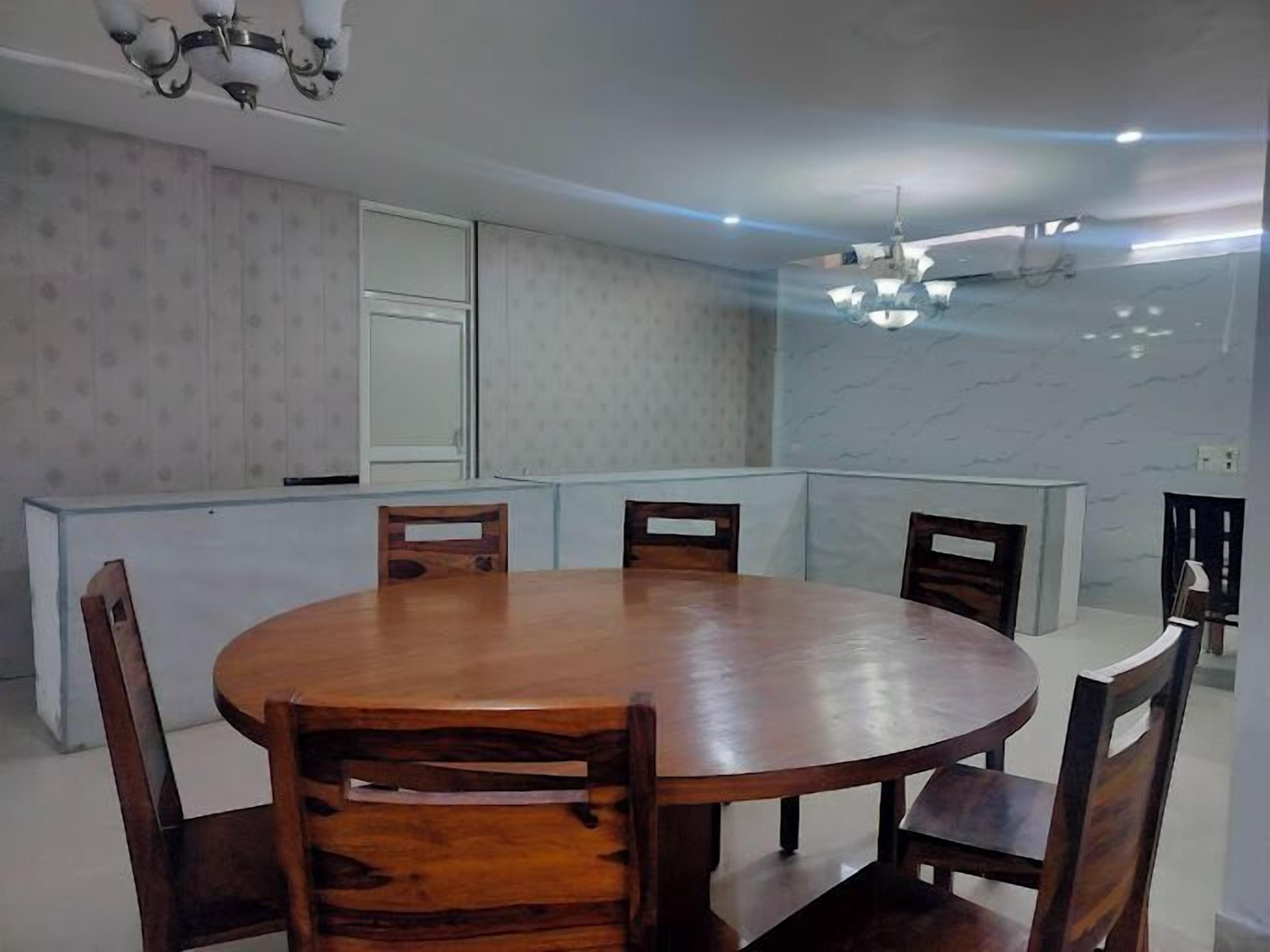 Uma área de refeições com uma mesa de madeira redonda e seis cadeiras, um armário branco e um ventilador de teto.