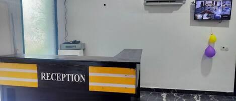 A reception desk with a 'RECEPTION' sign, a wall-mounted air conditioner, and a television displaying a video.