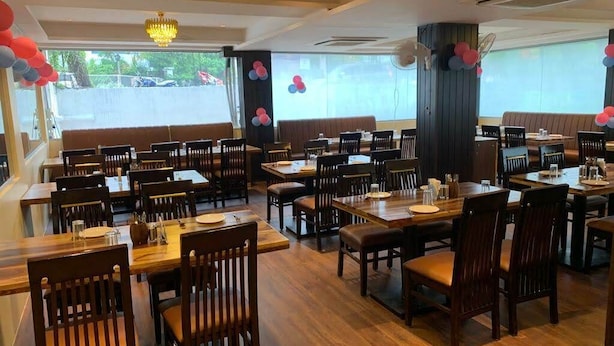 En restaurang med många bord och stolar, stora fönster och en kristallkrona.