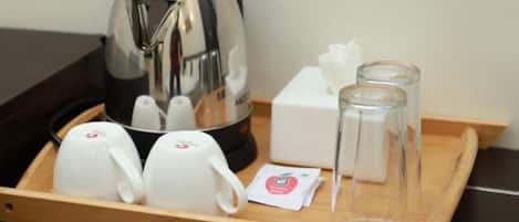 A tray with a stainless steel coffee maker, two white cups, two clear glasses, a tissue box, and a small packet.