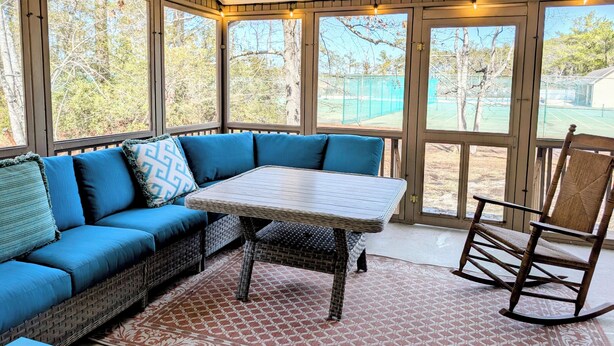 A sunroom with a blue sofa, wicker table, and rocking chair.