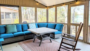 A covered porch with a blue sofa, a wicker table, and a rocking chair.