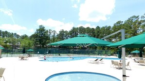 A swimming pool area with multiple pools, lounge chairs, and umbrellas.