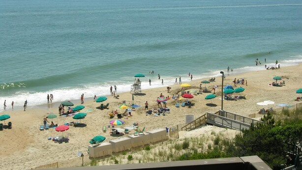 Een strand met meerdere parasols en ligbedden, een uitkijktoren voor strandwachten en een houten looppad naar het strand.