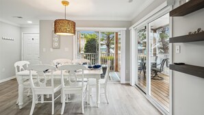 Een eetruimte met witte stoelen en een tafel, een hanglamp en uitzicht door glazen deuren op een terras.