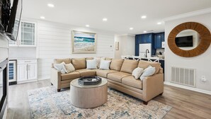 Een moderne woonkamer met een beige hoekbank, een salontafel en een groot schilderij van een zandstrand.