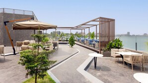 An outdoor patio area with seating arrangements, a pergola structure, and a view of the water. - Bickley Park Hotel (Lekki)
