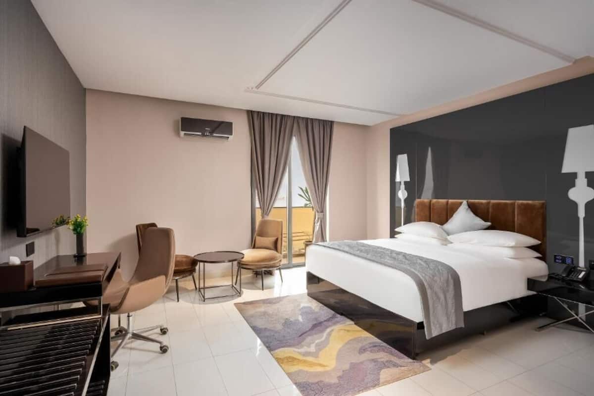 A modern hotel room with a large bed, a desk, a chair, and a TV.