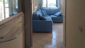 A living room with a large sectional sofa, a glass cabinet, and a view through a window with curtains. - Charming 1-bedroom apartment in Lerici with WiFi, AC (Lerici)