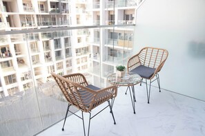 A balcony with two wicker chairs and a glass table, overlooking a high-rise building with multiple balconies. - Bloomfields Studio in Oasis 1 - Masdar (Abu Dhabi)