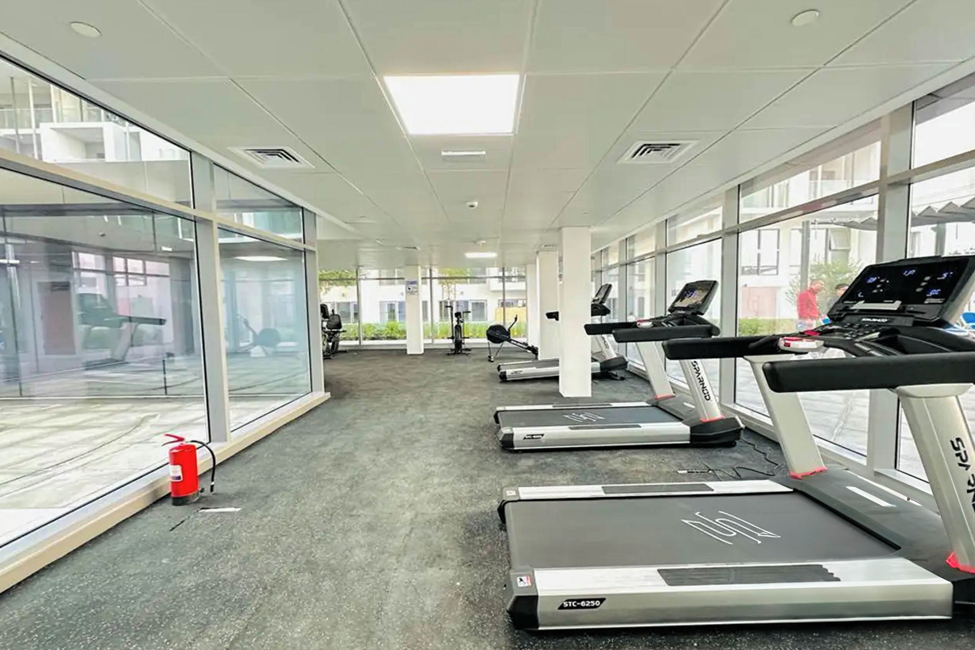 A gym with treadmills, exercise equipment, and large windows offering views of the outside.