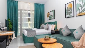 A modern hotel room with a bed, green sofa, round wooden table, and a dining area with a table and chairs. - Bloomfields Grandeur STU in Oasis Masdar (Abu Dhabi)