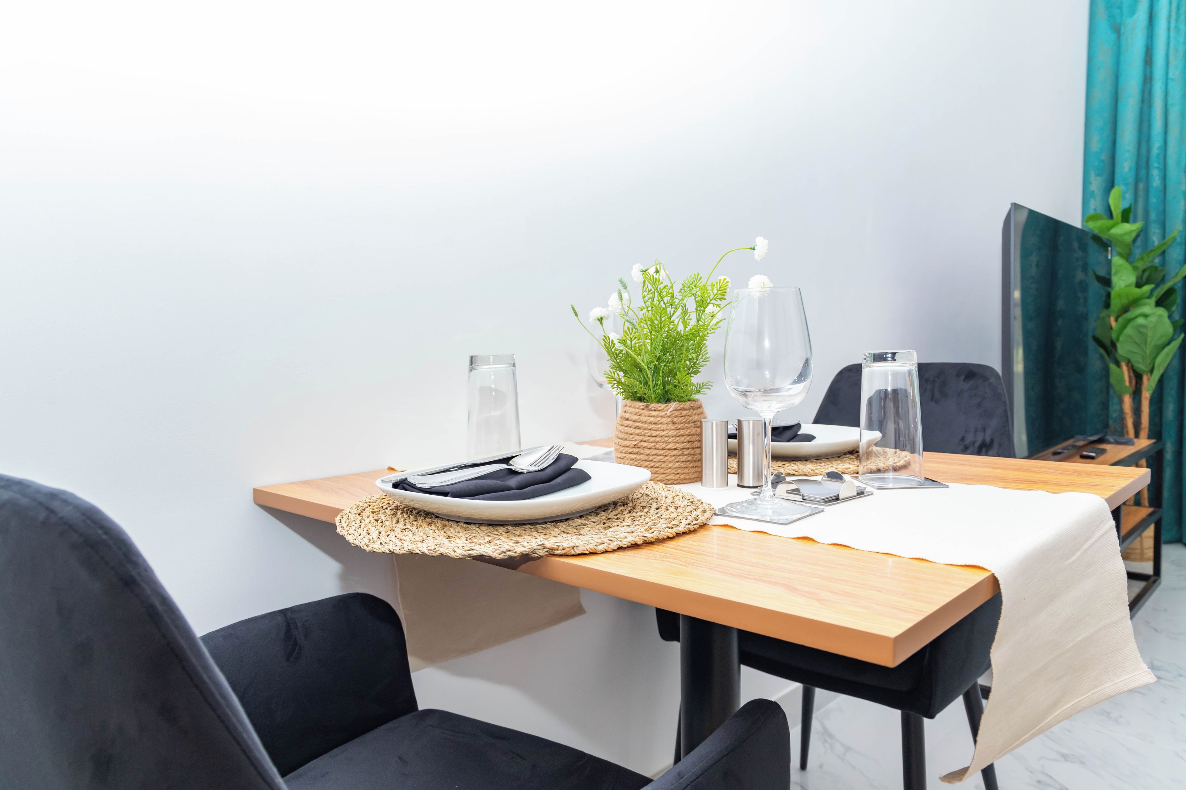 A dining table set with plates, cutlery, glasses, and a woven placemat.