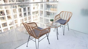 A balcony with two wicker chairs and a glass table, overlooking a high-rise building with multiple balconies. - Bloomfields Grandeur STU in Oasis Masdar (Abu Dhabi)