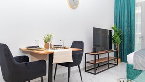 A modern hotel room with a dining area, a flat-screen TV, a bed, and a large window with curtains. - Bloomfields Grandeur STU in Oasis Masdar (Abu Dhabi)