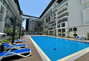 A modern hotel with a central swimming pool, sun loungers, and a multi-story building with balconies. - Bloomfields Grandeur STU in Oasis Masdar (Abu Dhabi)