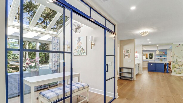 A modern kitchen with a blue island, white cabinets, and a view of the garden through a glass door. - FULLY RENOVATED, Gorgeous 3 Bedroom Sea Pines Home - Private Pool - Golf View (Hilton Head Island)