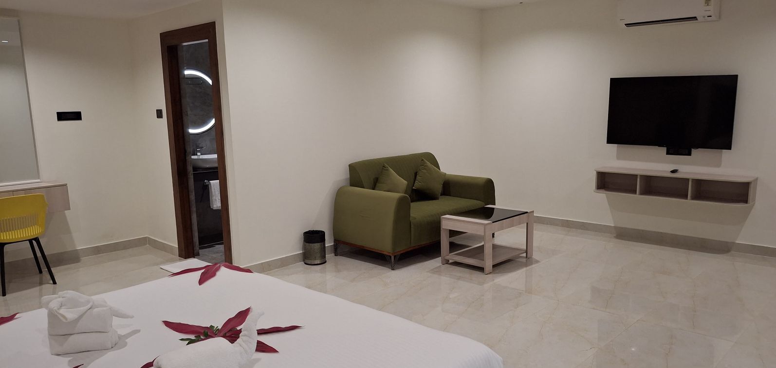 Una camera d'hotel moderna con un letto, un divano verde, un tavolino, una TV e uno specchio.