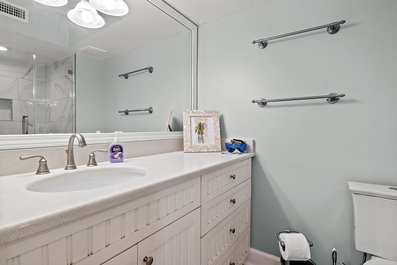 Une salle de bain avec un grand miroir, un lavabo blanc doté de deux robinets, des toilettes et un porte-serviettes.