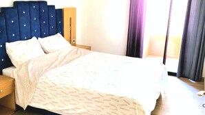 A hotel room with a large bed, a headboard, a nightstand, a bedside table, a wall-mounted air conditioner, and a window with curtains. - Apartment downtown Marrakech Guéliz (MARRAKECH)