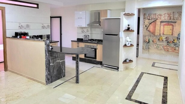 A modern kitchen with a marble island, stainless steel appliances, and a mural on the wall. - Apartment downtown Marrakech Guéliz (MARRAKECH)