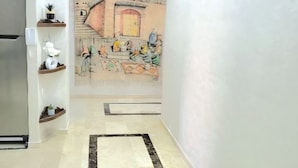 A hallway with a tiled floor, a refrigerator, wooden shelves with plants, and a mural on the wall. - Apartment downtown Marrakech Guéliz (MARRAKECH)