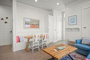 A room with white paneled walls, a wooden coffee table, a blue sofa, and a painting on the wall. - Charming Lakefront Cottage with Breathtaking Views in Cinnamon Shore South (Port Aransas)