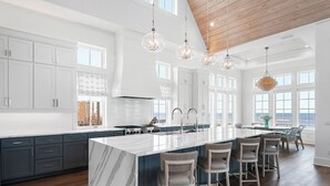 A spacious kitchen with a large island, dark wooden flooring, white cabinetry, and pendant lighting.