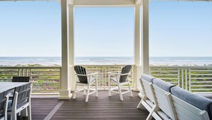 A covered deck with a view of the ocean, featuring a table, chairs, and a bench.