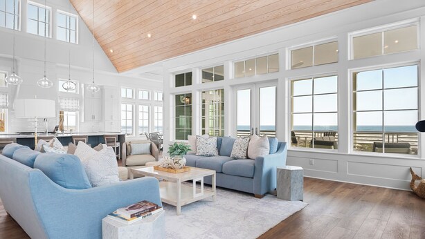 A spacious living room with a high ceiling, large windows, and a view of the ocean.