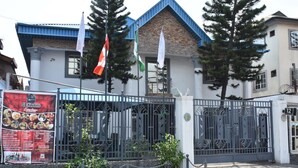 Un bâtiment doté d’une entrée fermée par un portail, de drapeaux et d’une enseigne.