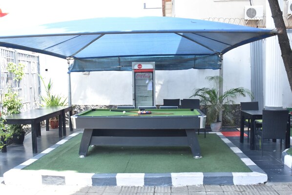 An outdoor pool table with a canopy, surrounded by chairs and tables, and a Coca-Cola vending machine. - SD HAVENS (Lagos)