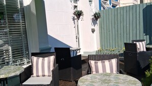 An outdoor patio with wicker furniture, a green umbrella, and potted plants. - The Barbican Hotel (Paignton)